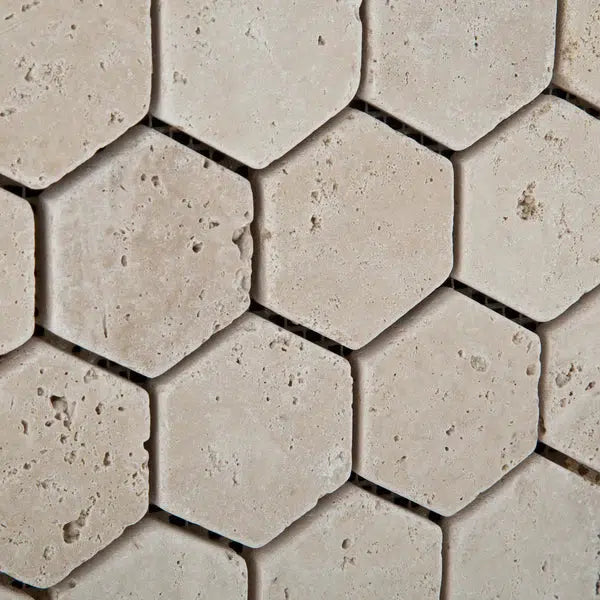 A close-up view of SurfacesGalore's Ivory (Light) Travertine 2X2 Hexagon Mosaic Tumbled tiles showcases their slightly rough texture and interlocking pattern. The naturally occurring small holes and imperfections add to the rustic charm and beauty of the beige tiles.