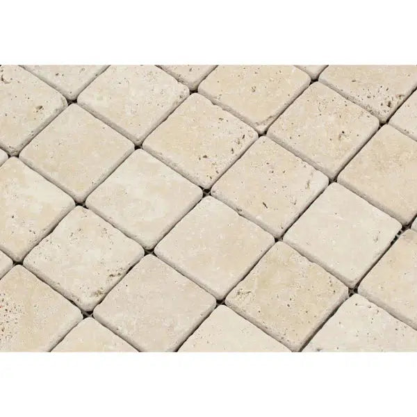 Close-up of SurfacesGalore's Ivory (Light) Travertine 2X2 Mosaic Tumbled tiles arranged in a diagonal grid. The square-shaped tiles exhibit a slightly rough texture, with natural variations in color and surface markings.