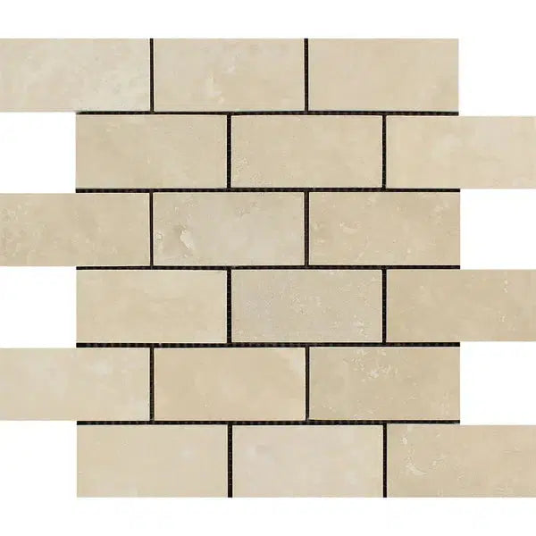 A close-up image of beige brick-patterned Ivory Travertine tiles from SurfacesGalore, specifically the Ivory (Light) Travertine 2X4 Brick Mosaic Filled and Honed. The tiles feature slightly varied shades and natural textures, arranged in a staggered, horizontal layout with thin dark grout lines separating each tile.