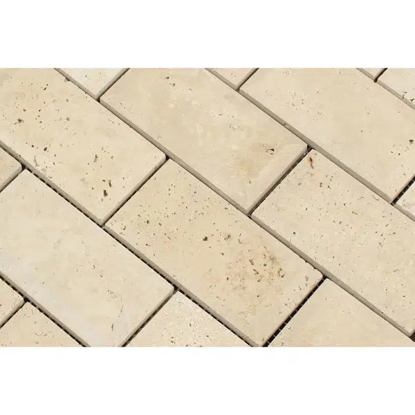 Close-up view of a beige rectangular brick pattern made from SurfacesGalore's Ivory (Light) Travertine 2X4 Deep-Beveled Brick Mosaic Honed tiles. The tiles have a textured surface with small brown specks and color variations, giving them a rustic appearance. They are arranged in a staggered, horizontal layout.