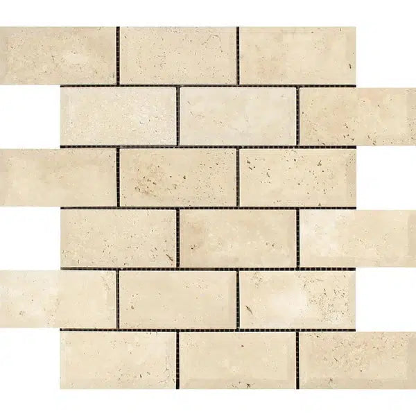 A pattern of beige rectangular tiles, known as Ivory (Light) Travertine 2X4 Deep-Beveled Brick Mosaic Honed, is arranged in a staggered brick layout. The tiles have a textured appearance with subtle variations in color and natural speckles, creating a rustic and earthy feel. The tiles are interspersed with thin, dark grout lines from SurfacesGalore.