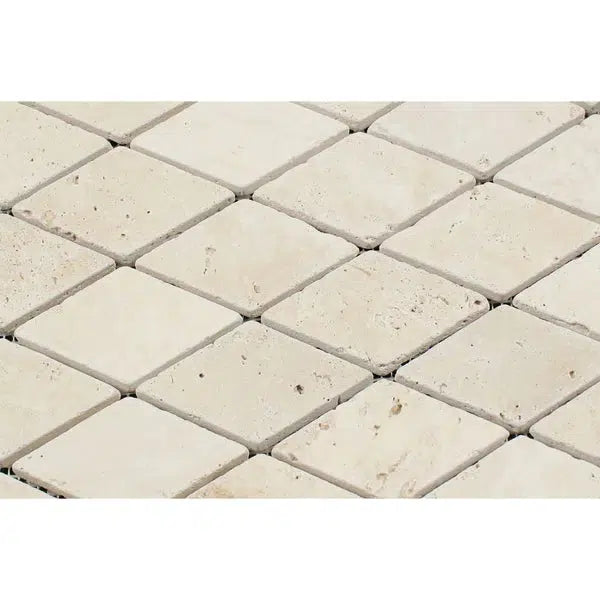 A close-up view of the Ivory (Light) Travertine 2X4 Diamond / Rhomboid Mosaic Tumbled pattern by SurfacesGalore, showcasing square tiles with a slightly textured surface arranged in a diagonal grid. The tiles are evenly spaced with light grout filling the gaps in between.