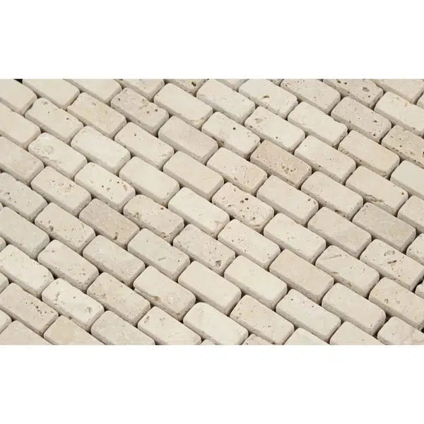 Close-up of Ivory (Light) Travertine 5/8X1 1/4 Mini-Brick Mosaic Tumbled tiles arranged in a diagonal, staggered pattern. The surface of these premium tiles appears slightly textured, showcasing natural stone variations in shades and small pits typical of travertine material. The image captures a uniform, repetitive design by SurfacesGalore.