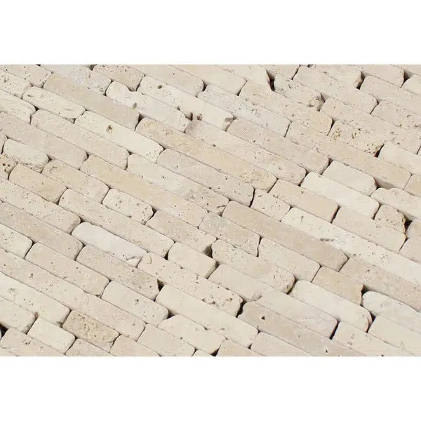 A close-up view of a textured surface made up of small, rectangular beige stones arranged in a diagonal, interlocking pattern. The slightly rough and porous Ivory (Light) Travertine Random Strip Mosaic Tumbled tiles enhance the natural and rustic look, showcasing the classic beauty found at SurfacesGalore.