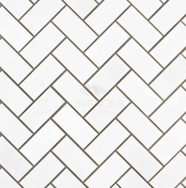 Thassos White (Greek) 1X2 Herringbone Mosaic Marble Polished-Honed tiles with grey grout lines create a chevron pattern, featuring the SurfacesGalore logo at the center.