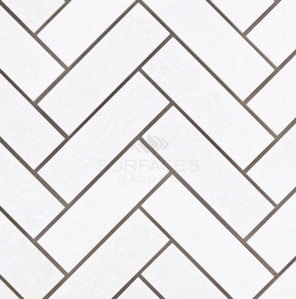 The herringbone pattern of SurfacesGalore's Thassos White (Greek) 1X3 Herringbone Mosaic Marble Polished-Honed tiles with gray grout lends a touch of elegance to any space.