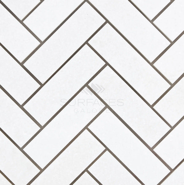 The herringbone pattern of SurfacesGalore's Thassos White (Greek) 1X3 Herringbone Mosaic Marble Polished-Honed tiles with gray grout lends a touch of elegance to any space.