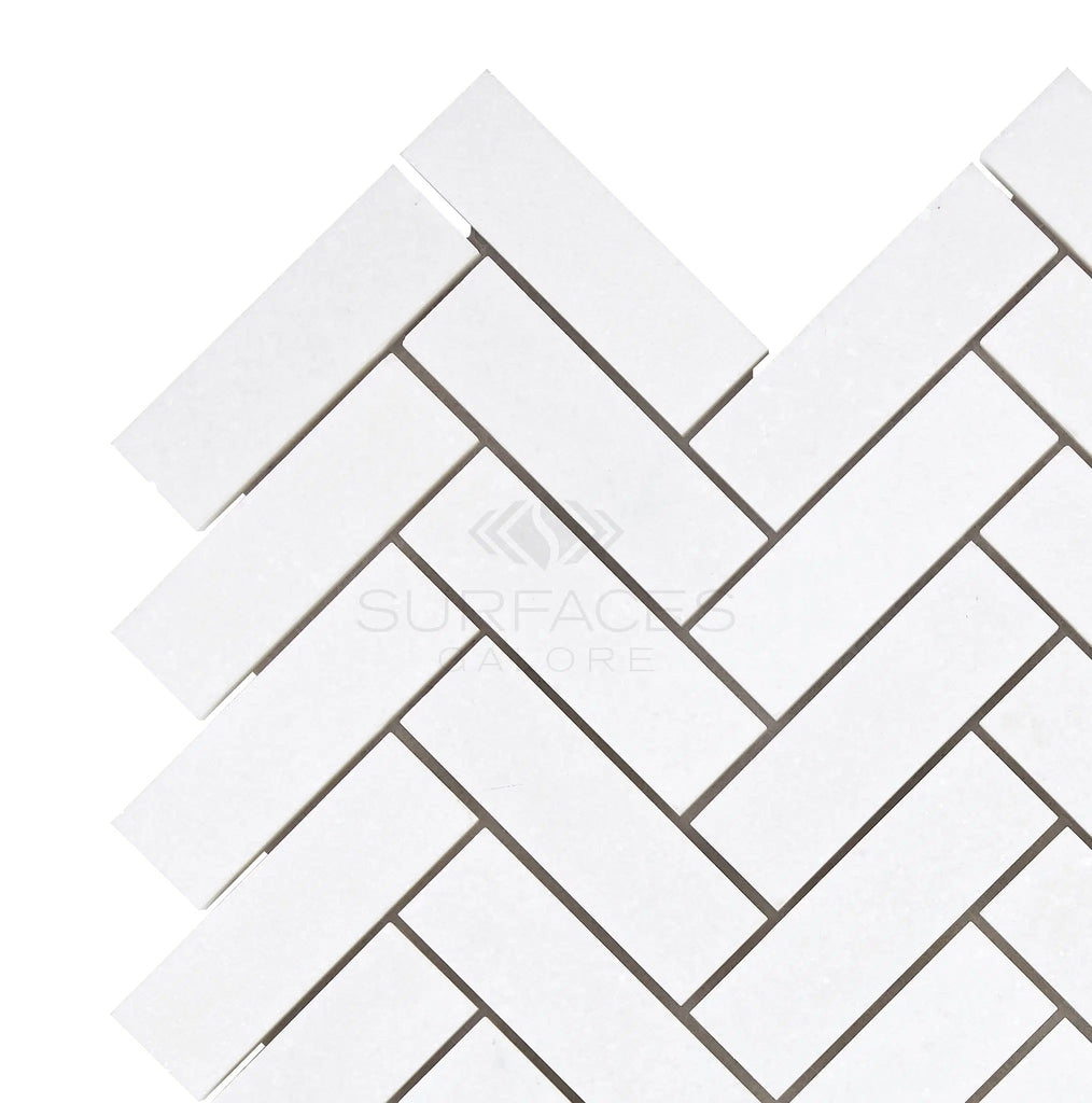 White rectangular tiles arranged in a herringbone pattern against a light background showcase the elegance of the Thassos White (Greek) 1X3 Herringbone Mosaic Marble Polished-Honed by SurfacesGalore, enhancing the pure white color of your space.