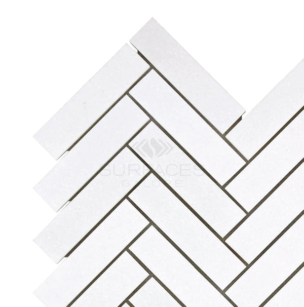 Thassos White (Greek) 1X4 Herringbone Mosaic Marble Polished-Honed from SurfacesGalore are beautifully arranged in a herringbone pattern on a flat surface, showcasing their pure white color reminiscent of Thassos White Marble.