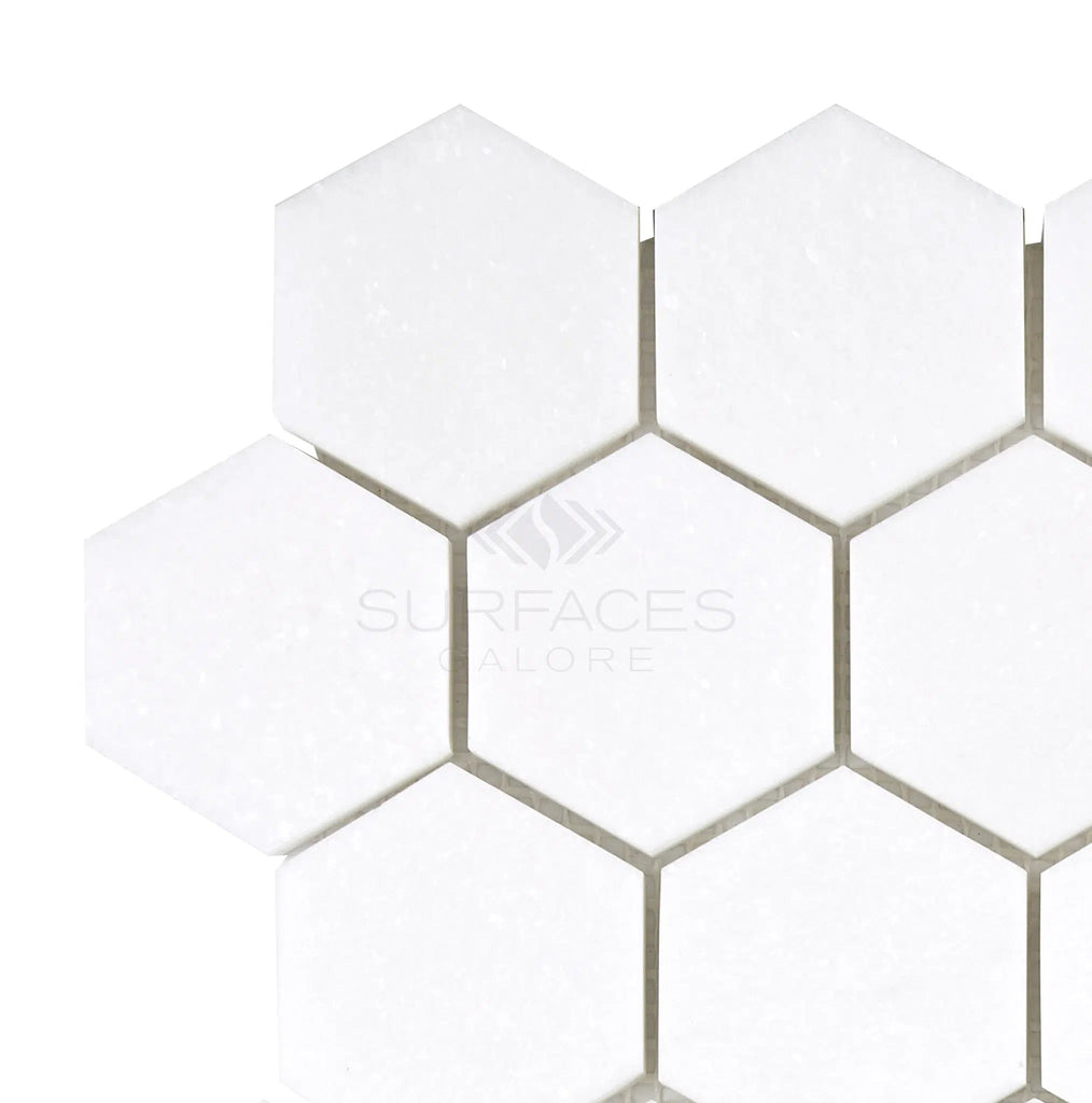 Hexagonal white tiles arranged in a honeycomb pattern with the text "SurfacesGalore" in the center, crafted from pristine Thassos White (Greek) 2X2 Hexagon Mosaic Marble Polished-Honed.