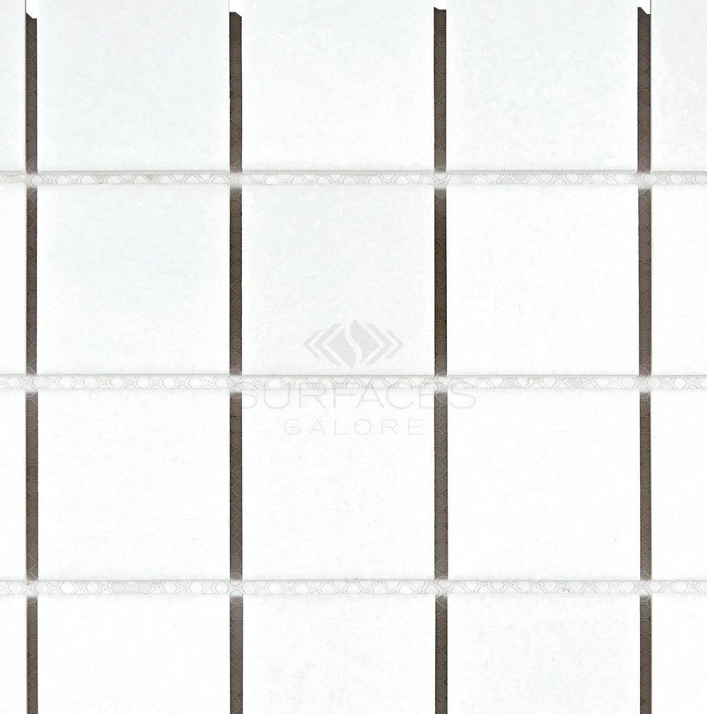 Close-up of a grid pattern featuring SurfacesGalore Thassos White (Greek) 2X2 Mosaic Marble Polished-Honed tiles with dark grout lines, showcasing a refined crystalline texture.