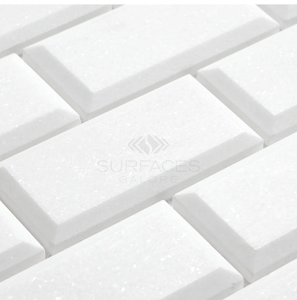 White, rectangular Thassos White (Greek) 2X4 deep-beveled brick mosaic marble tiles with a polished-honed finish, arranged in a staggered pattern. Text reads "SurfacesGalore," offering a luxurious look reminiscent of Thassos White Marble.