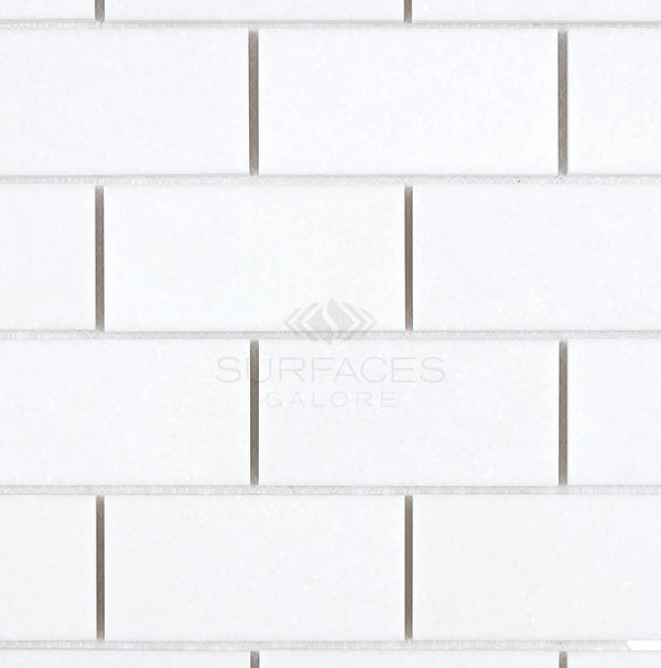 The Thassos White (Greek) 2X4 Straight-Edged Brick Mosaic Marble Polished-Honed tiles, emblazoned with the SurfacesGalore logo, feature a sleek arrangement in a classic brick pattern. These sophisticated tiles capture the luxurious essence of Thassos White Marble, reflecting the enduring elegance of Greek marble aesthetics.