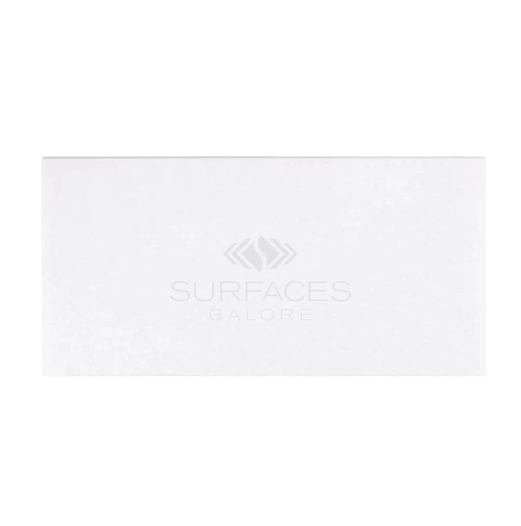 Rectangular white tile with subtle textures, featuring the SurfacesGalore logo in the center. The refined crystalline texture evokes the elegance of Thassos White Marble, adding a touch of sophistication to any space. This is the Thassos White (Greek) 3X6 Marble Polished-Honed from SurfacesGalore.