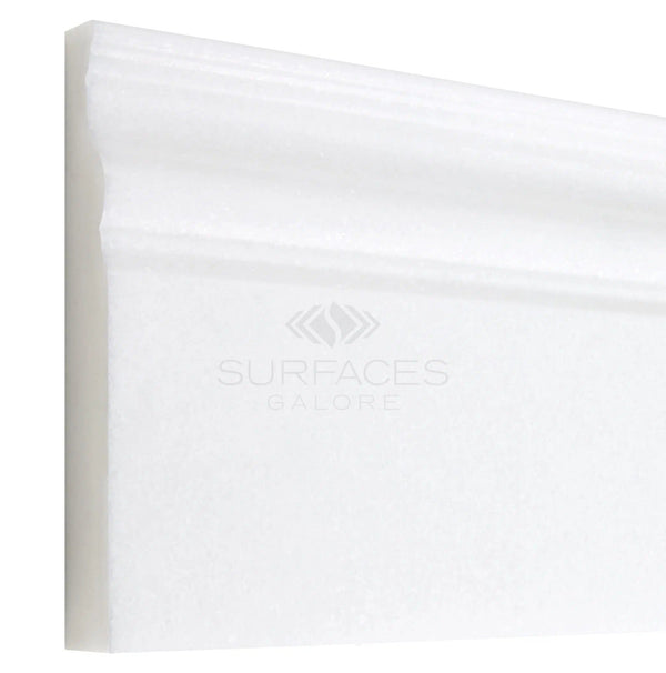 The Thassos White (Greek) 4 3/4X12 Baseboard Trim Marble Polished-Honed by SurfacesGalore features a simple design and a pure white color reminiscent of Thassos White Marble. The "SurfacesGalore" text is lightly visible on the trim.