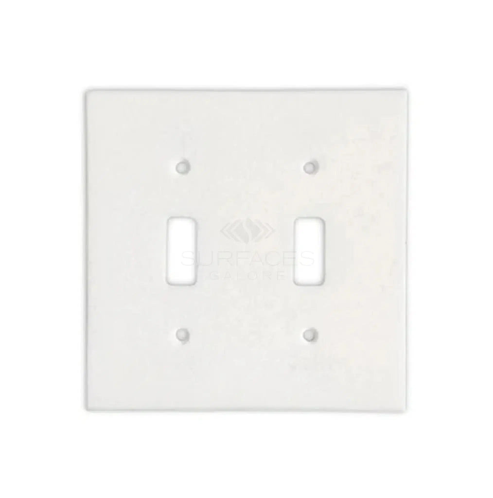 A luxurious home decor piece, the Thassos White Marble Double TOGGLE Switch Wall Plate from SurfacesGalore features two rectangular openings for switches, blending seamlessly into a pristine white background.