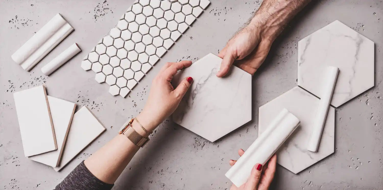 Two people arranging hexagonal and rectangular white ceramic tiles on a gray surface.