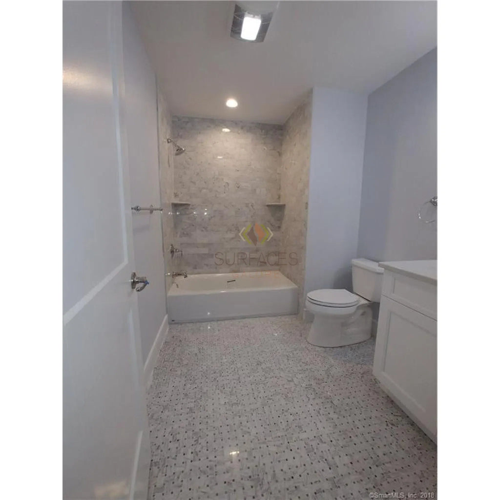 Elegant Bathroom Featuring Carrara White Trim Molding with Tub and Toilet Setup