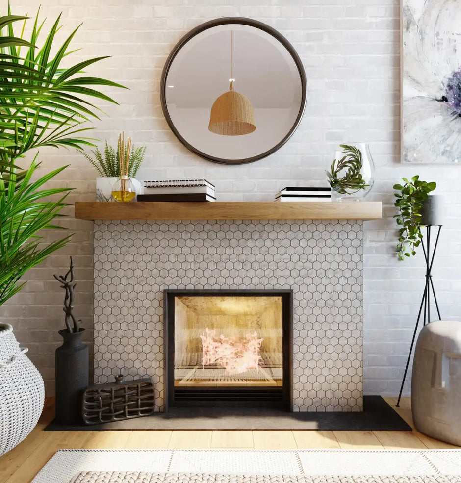 A cozy living room features a tiled fireplace, wooden mantel, round mirror, potted plants, books, and modern decor.