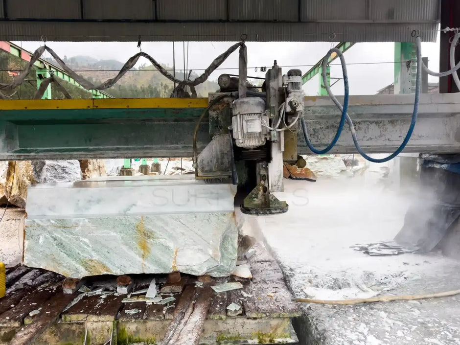 A stone cutting machine processing a large block of stone in an industrial setting, surrounded by mist and debris.