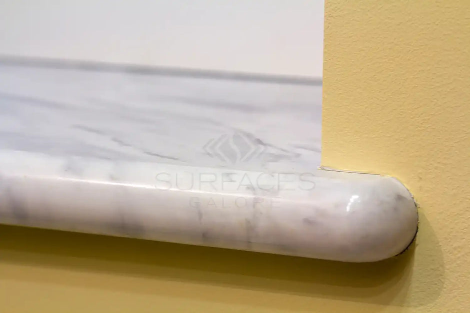 Close-up of a marble countertop with rounded edges positioned against a yellow wall.