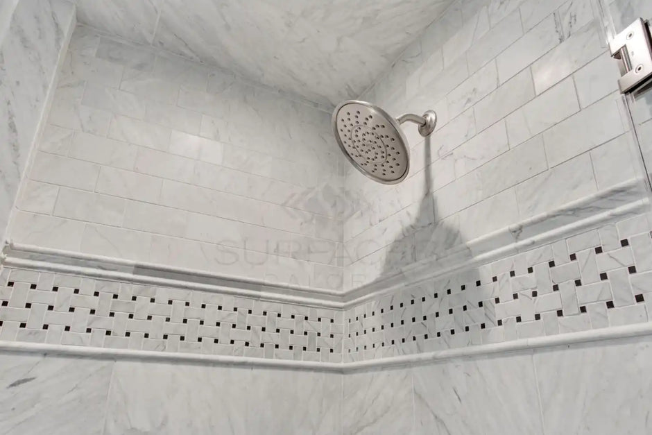 Close-up of a shower with a silver showerhead and light gray tile walls featuring decorative horizontal patterns.