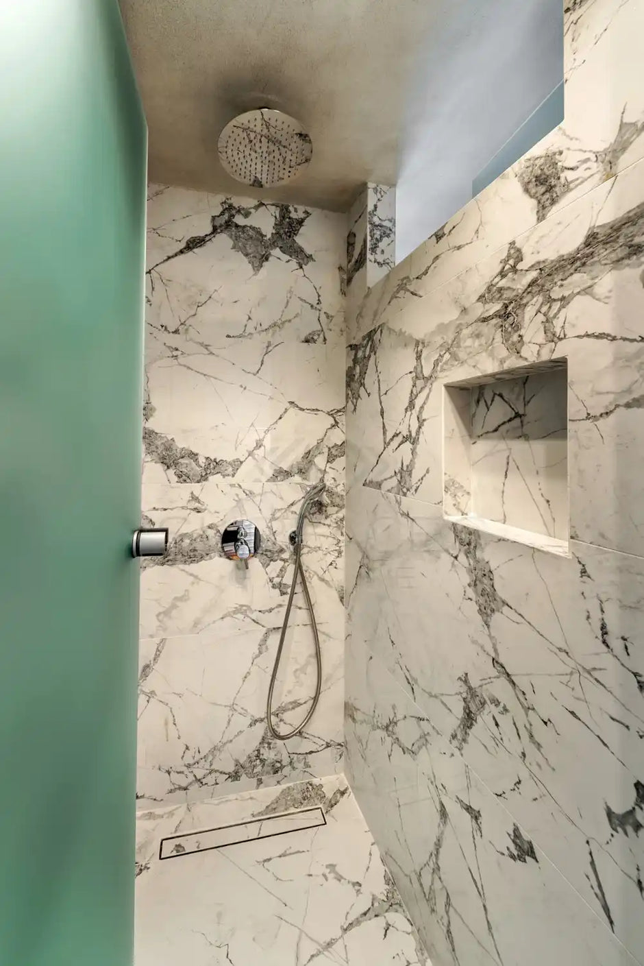 A modern shower with a rain showerhead, marble walls, and a built-in niche, featuring a frosted glass door.