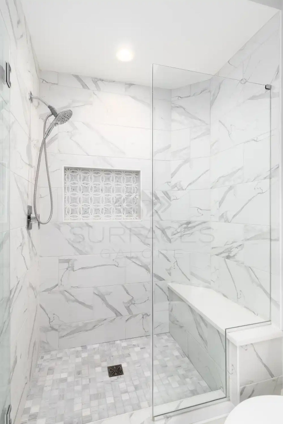 Modern, white marble shower with built-in niche, bench, rain showerhead, and glass door.