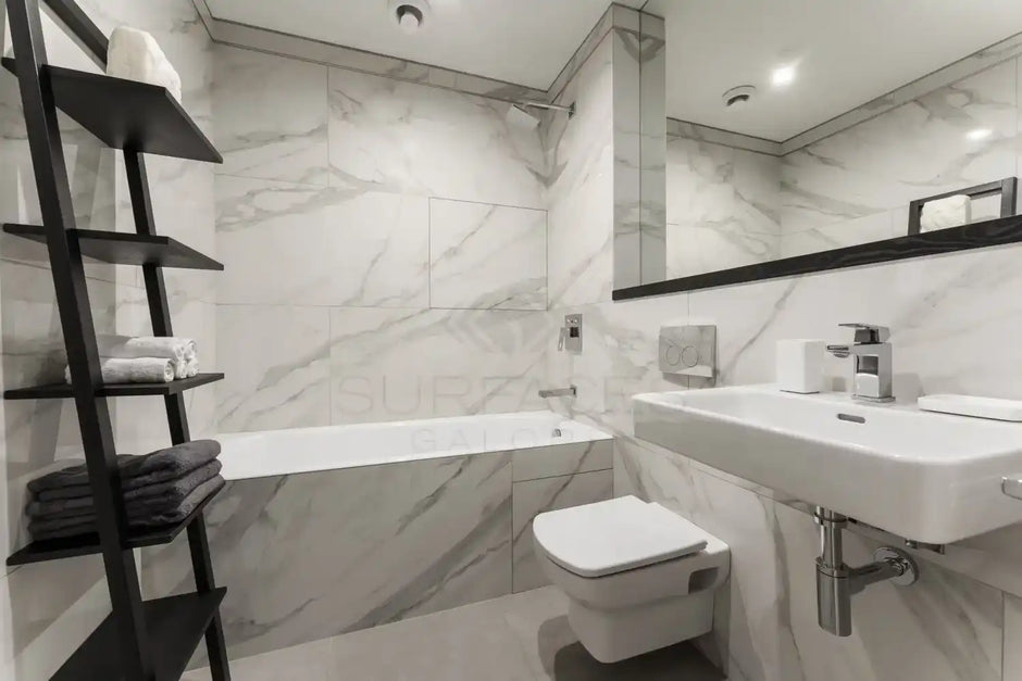 Elegant, modern bathroom with marble walls, floating sink, wall-mounted toilet, bathtub, large mirror, and shelves.