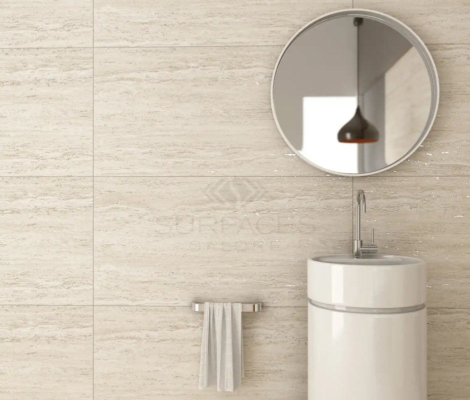 Minimalist bathroom with round mirror, small sink, and towel on rail against beige tiled wall.