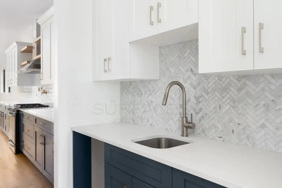 Modern kitchen with white and dark blue cabinetry, stainless steel fixtures, and herringbone tile backsplash.