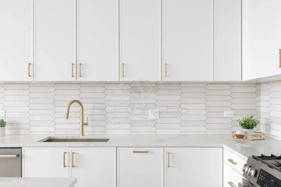 Modern kitchen with white hexagonal tile backsplash, white cabinets with gold handles, and a gold faucet.