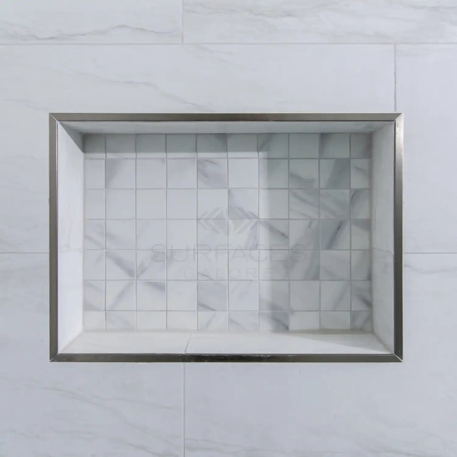 A recessed shower niche with a stainless steel frame, tiled with white and grey marble squares.