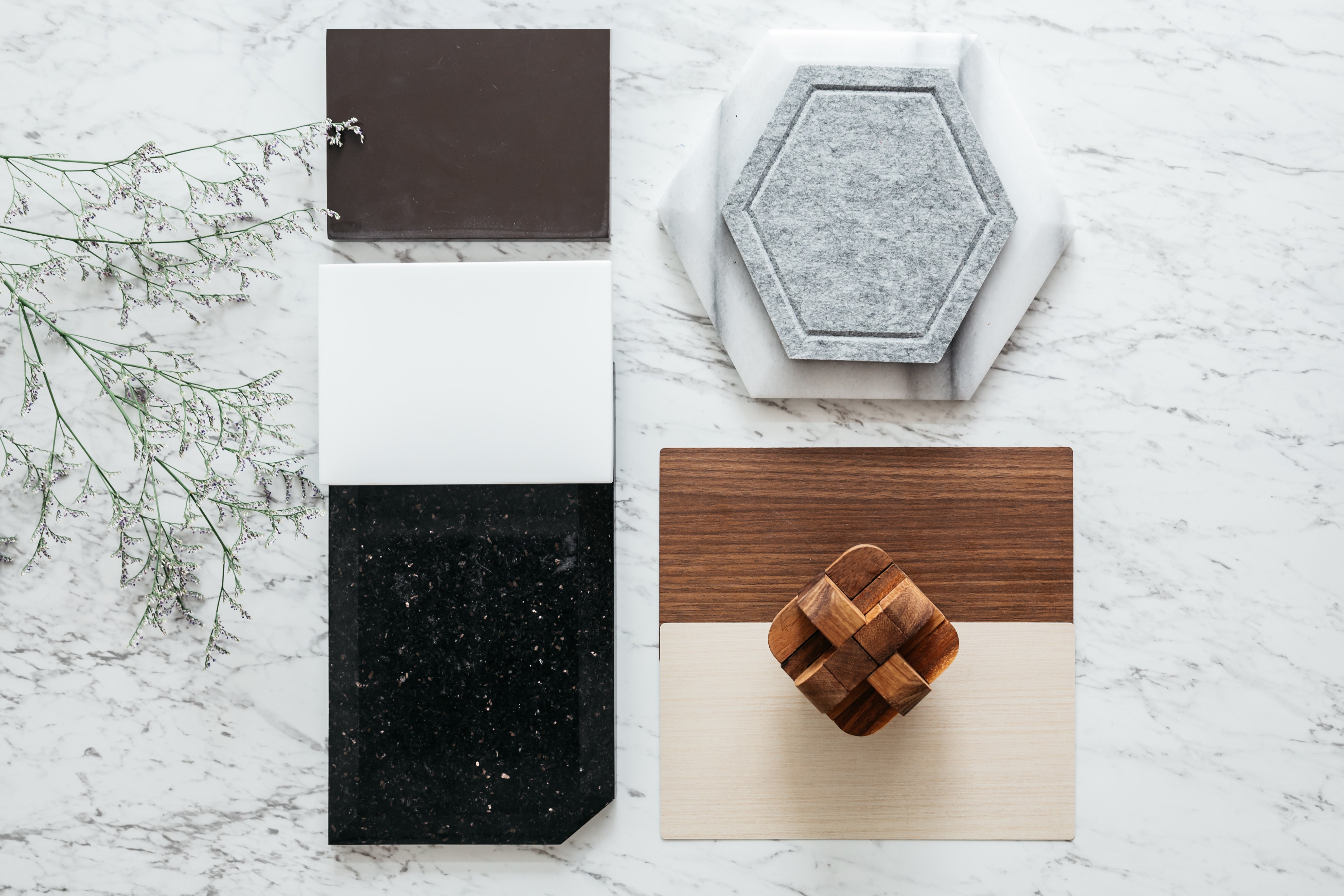 A collection of square and hexagonal tiles with varied textures and colors, placed on a marble surface next to a plant.