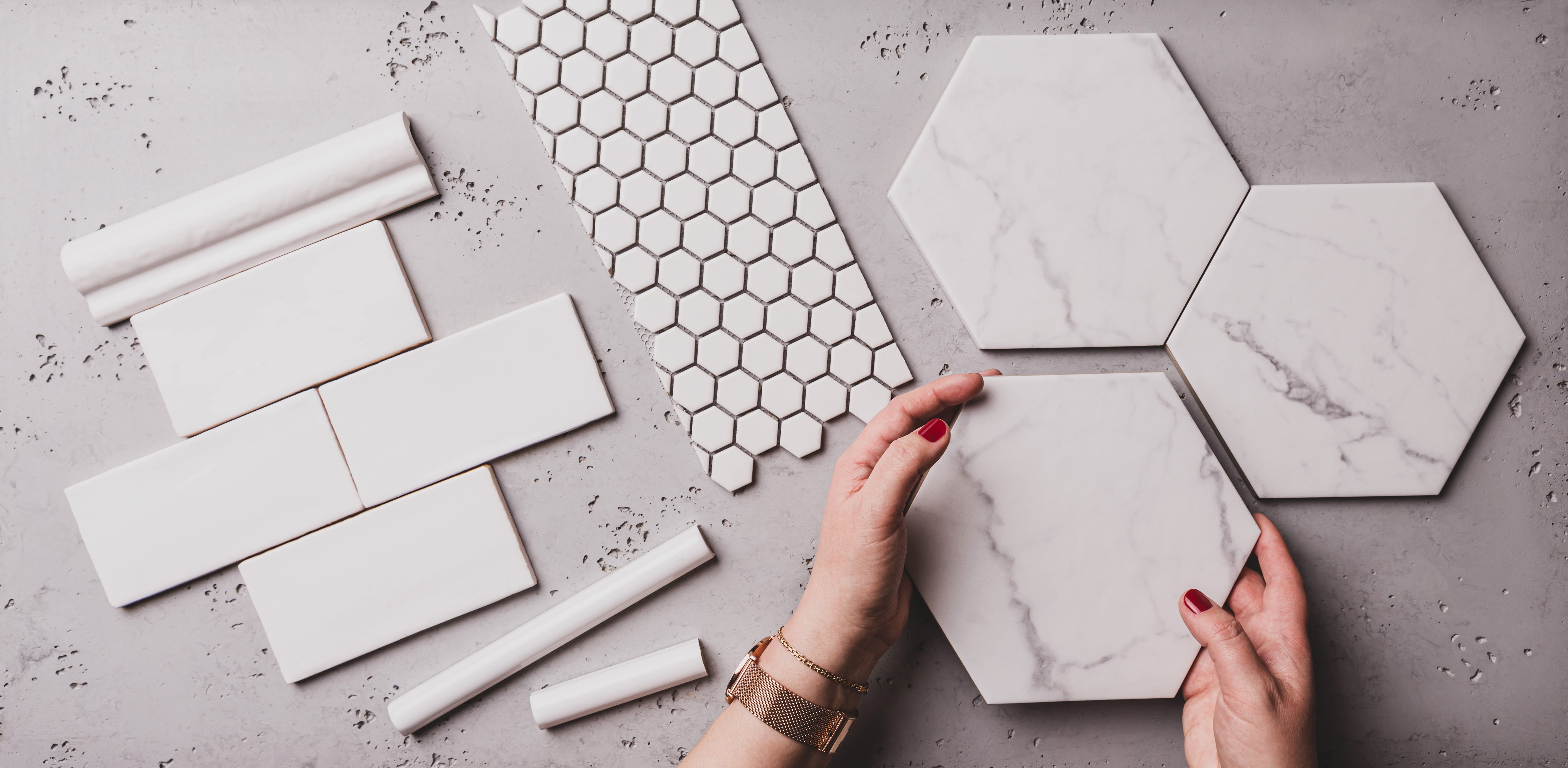 Hands holding hexagon marble tiles on a gray background, with various white tiles arranged around.