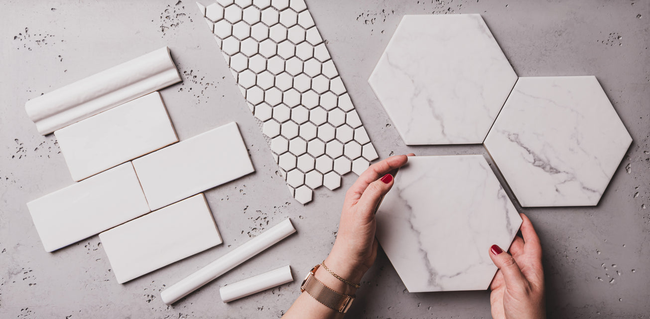 Hands holding large white hexagonal tiles on a surface with various other white tiles and patterns.