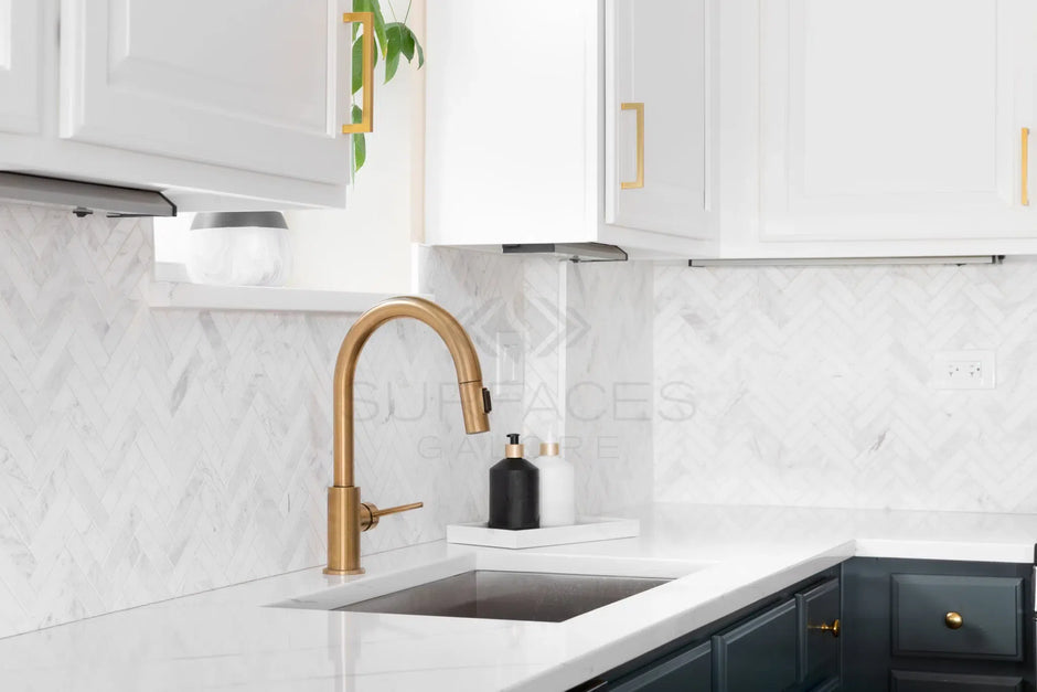 Modern kitchen with white cabinets, marble backsplash, a gold faucet, and dark lower cabinets. Natural light from window.