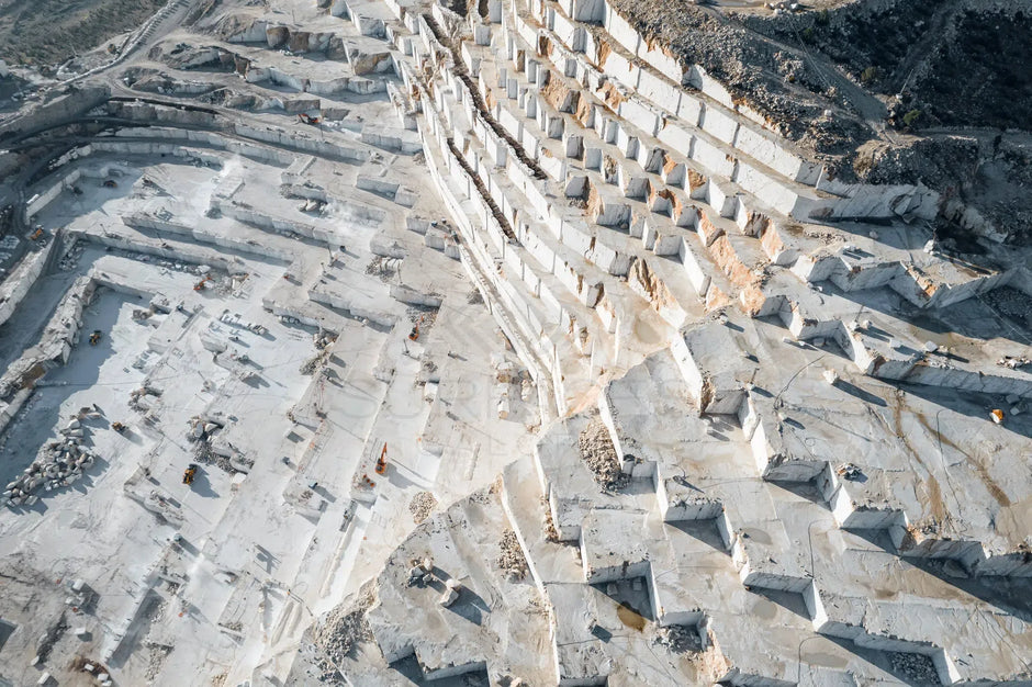 Aerial view of a large, stepped marble quarry with white stone and various levels of excavation.