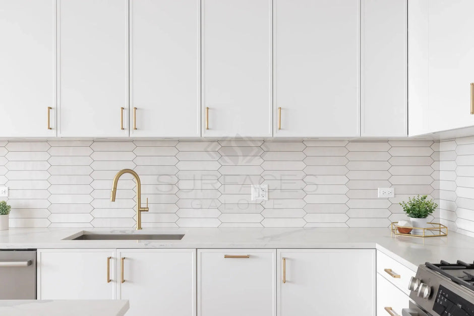 Modern kitchen with white hexagonal tile backsplash, white cabinets with gold handles, and a gold faucet.