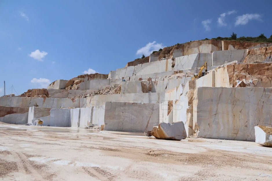 A marble quarry with large, white stone blocks and machinery against a clear blue sky.