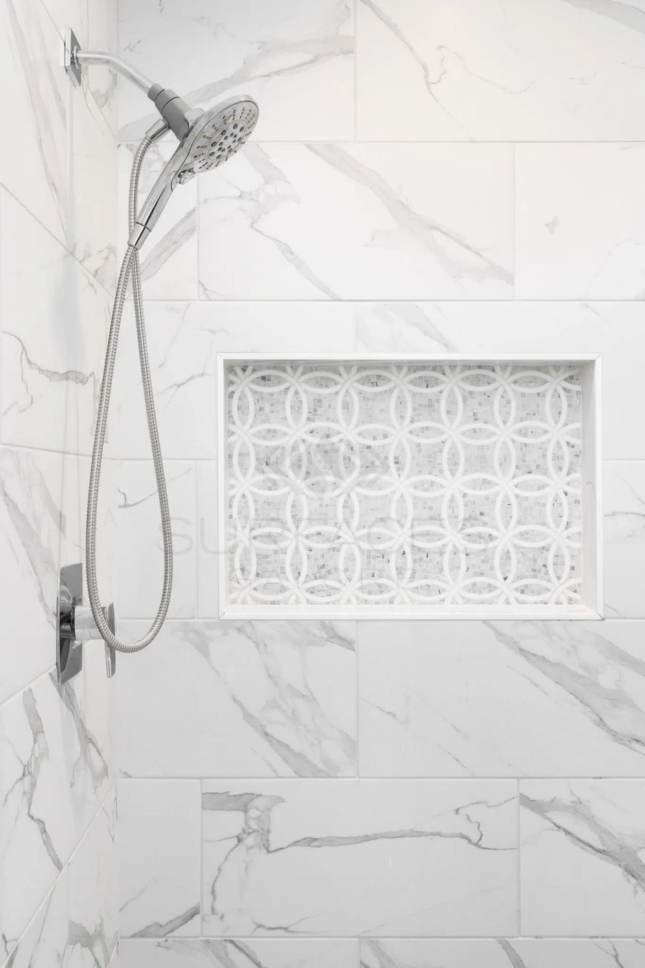 Marble-tiled shower with a built-in niche featuring decorative tile, a handheld showerhead, and silver fixtures.