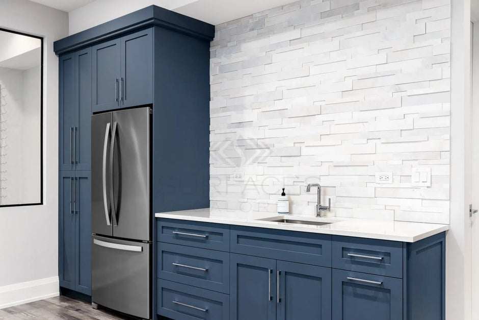 Modern kitchen with blue cabinets, stainless steel refrigerator, white countertop, and white textured backsplash.