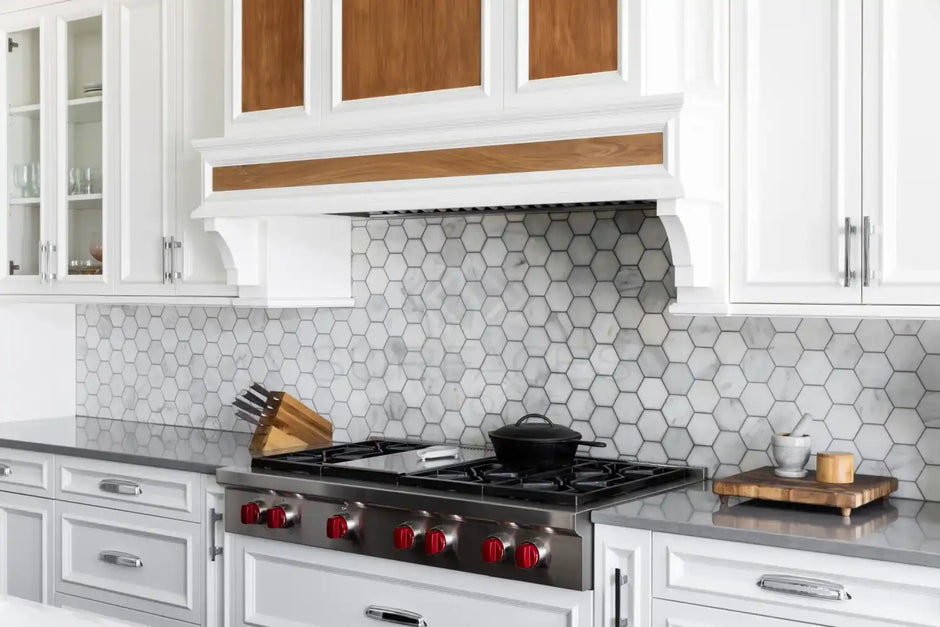 Modern kitchen with hexagonal tile backsplash, stainless steel stove with red knobs, white cabinetry, and wooden accents.