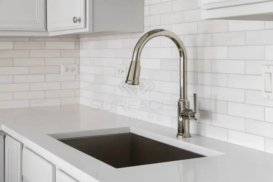 Modern kitchen sink with a sleek stainless steel faucet, white countertops, and white tiled backsplash.