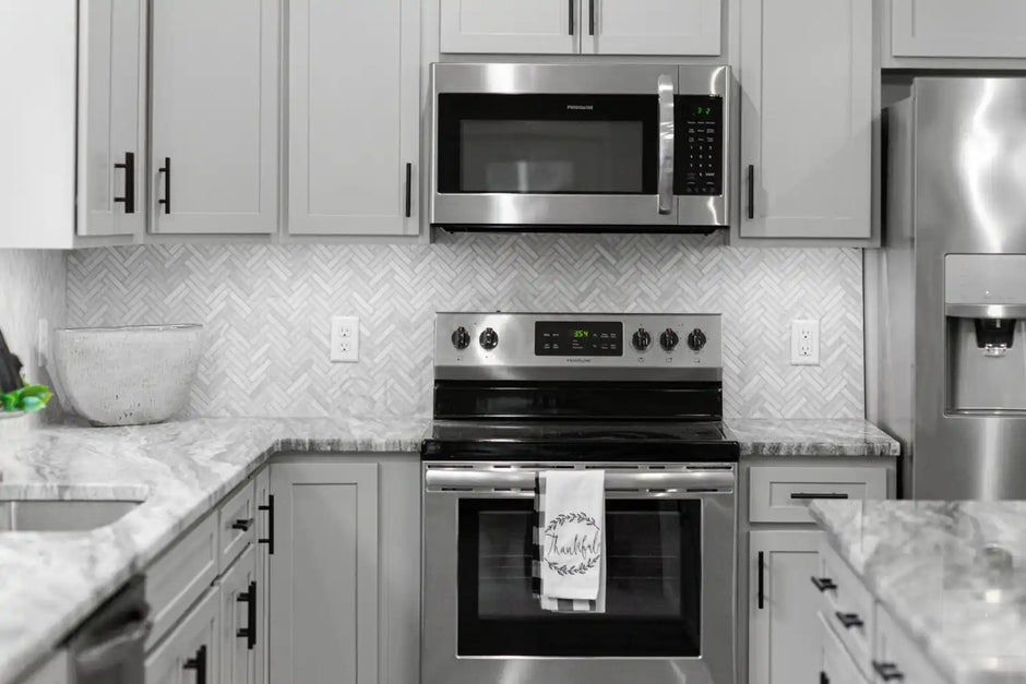 Modern kitchen with gray cabinets, stainless steel appliances, herringbone tile backsplash, and marble countertops.