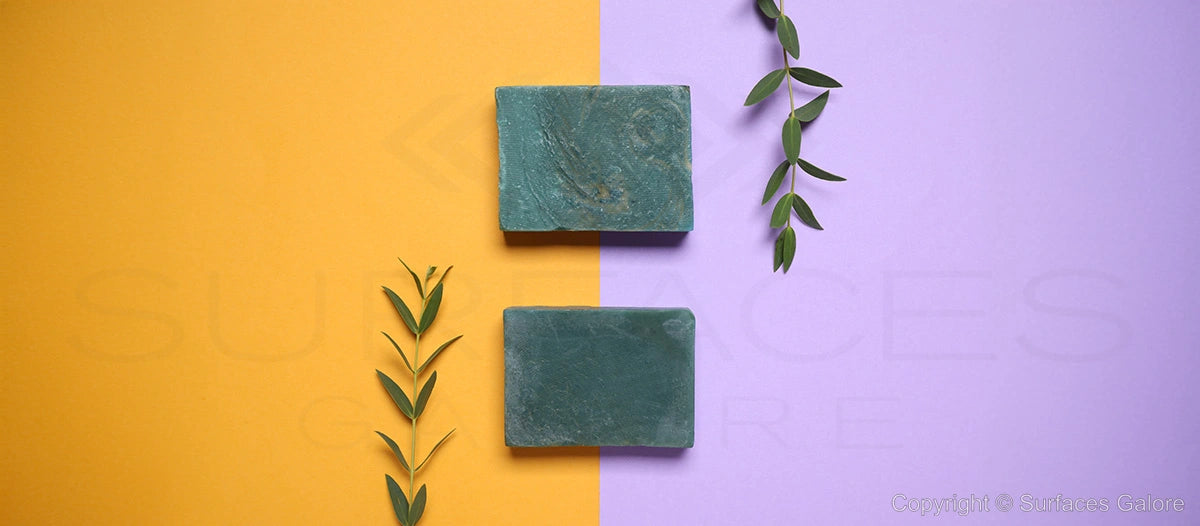 Two rectangular green soap bars are displayed on a background split into yellow on the left and lavender on the right. Olive leaves are arranged vertically next to each soap bar, enhancing the natural and refreshing theme.