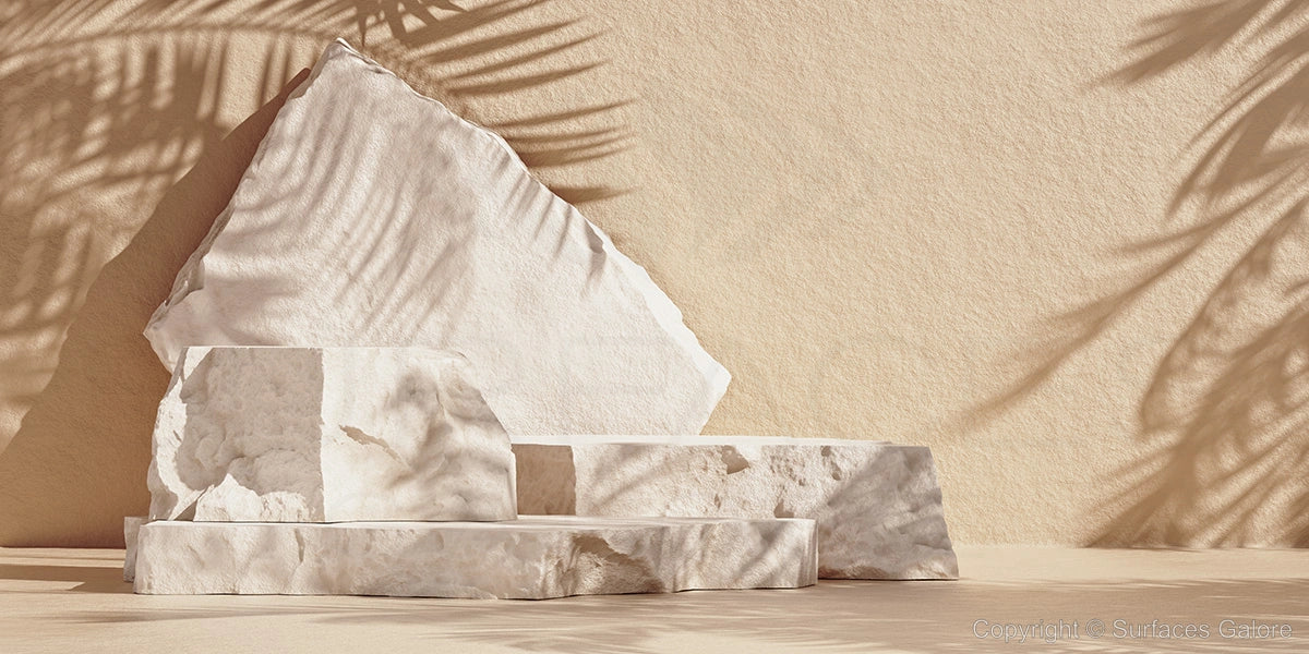 Several large, irregularly shaped white stone slabs are stacked against a beige background. The image features soft shadows of palm fronds cast on the stones and background, adding a natural and serene touch.