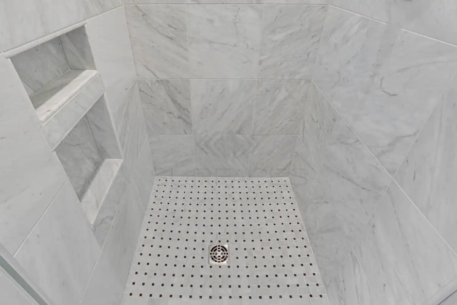 Marble-tiled shower with built-in shelves and a square mosaic tile floor with a drain in the center.